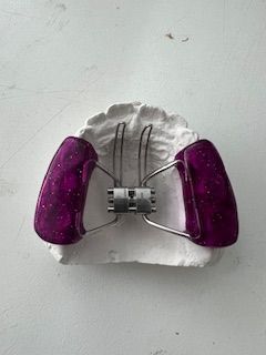 A close up of a purple dental device on a white surface.