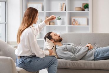 A therapist in a white shirt holds a pendulum over a person lying on a couch during a hypnotherapy session. A therapist in a white shirt holds a pendulum over a person lying on a couch during a hypnotherapy session.