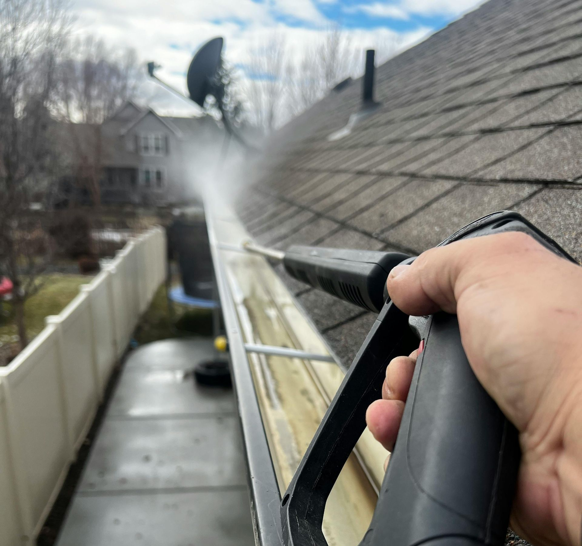 Person using a pressure washer to clean a gutter on a house.