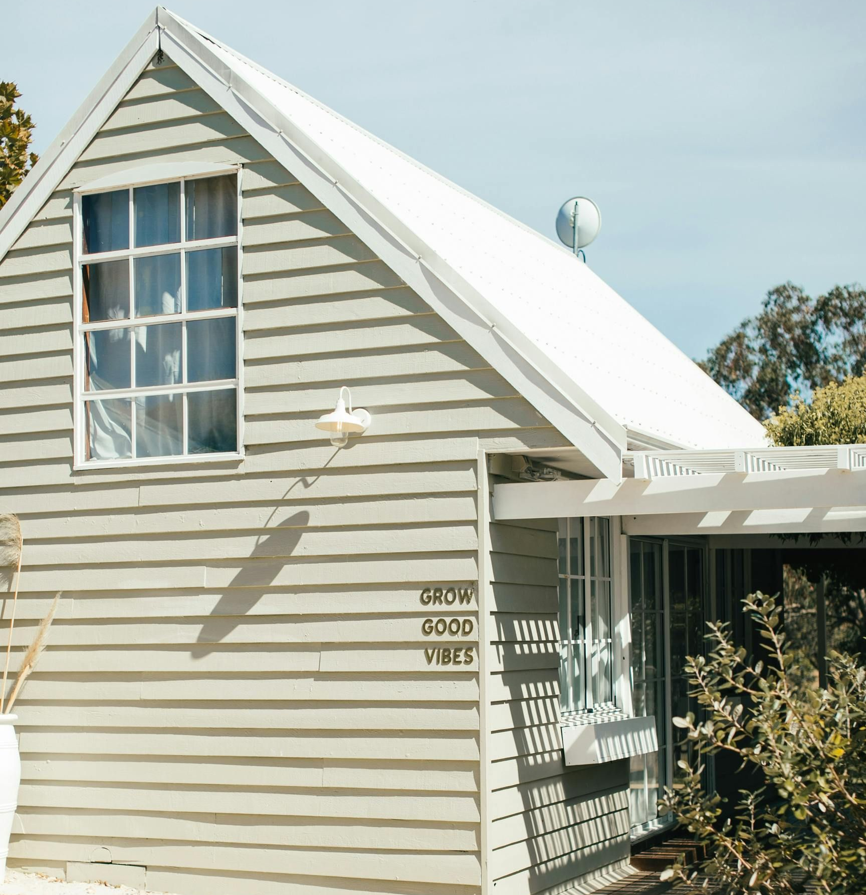 Gray and white cottage with a sloped roof and a large window, “good vibes” text on the side.