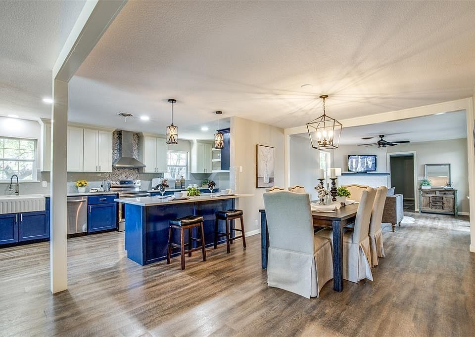 Open-concept kitchen and dining room with blue island, white chairs, and hardwood floors