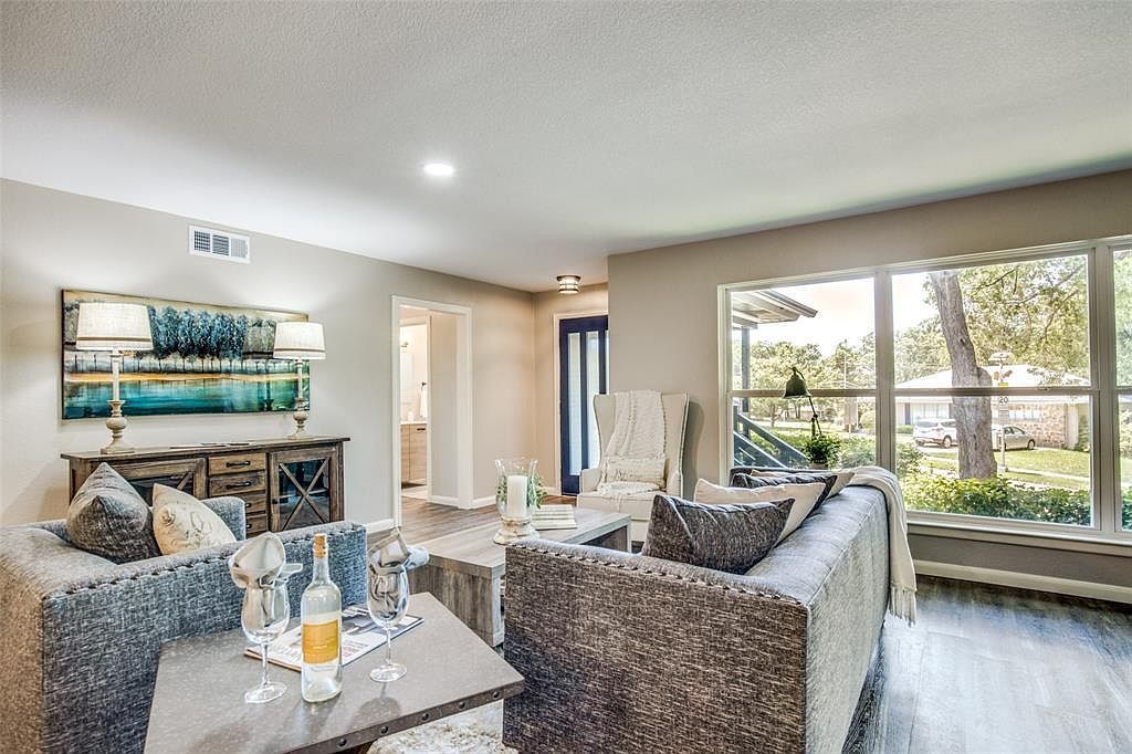 Bright modern living room with gray sofas, coffee table, wall art, and large windows overlooking trees.