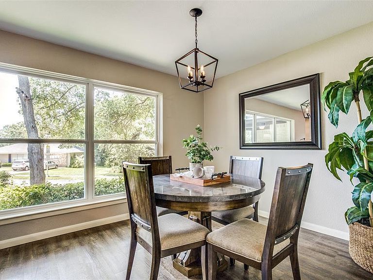 Bright dining nook with round table, four chairs, large windows, mirror, and indoor plant.