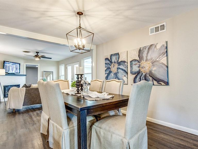 Dining room with dark wood table, cream chairs, floral wall art, and a chandelier in a bright open floor plan.