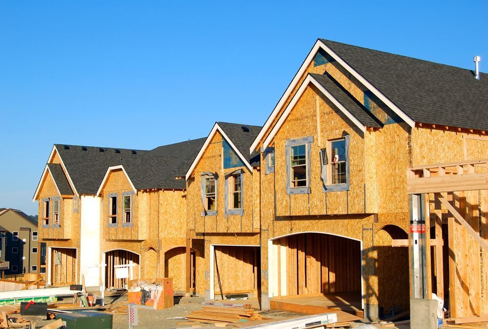 Row of unfinished wooden houses under construction against a clear blue sky