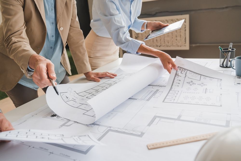 People reviewing architectural blueprints on a table, with one person unrolling plans and another holding a ruler.