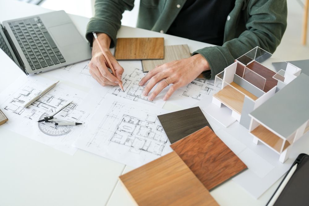 Designer sketching floor plans with wood samples and laptop on a desk