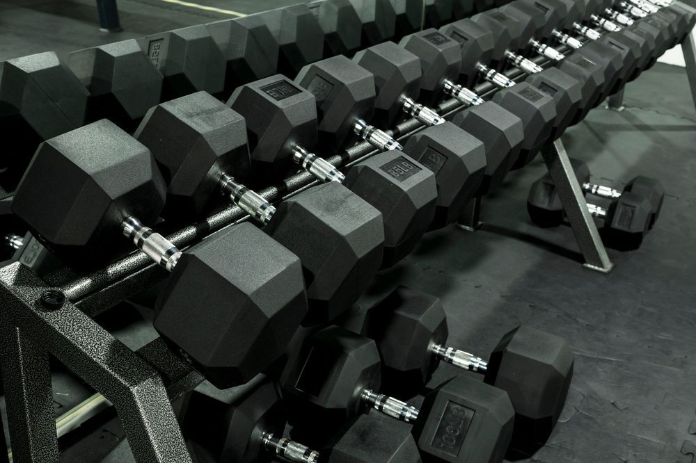 Rows of black hex dumbbells stacked on a gym rack, viewed at an angle.