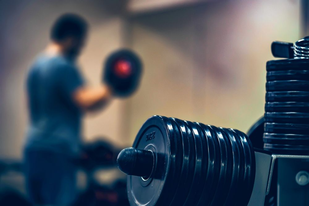 Person lifting a dumbbell in a gym, with stacked weights in the foreground.