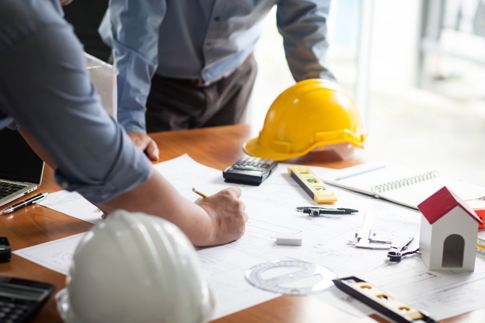 Architectural team reviewing plans with a yellow hard hat, tools, and house model on a table