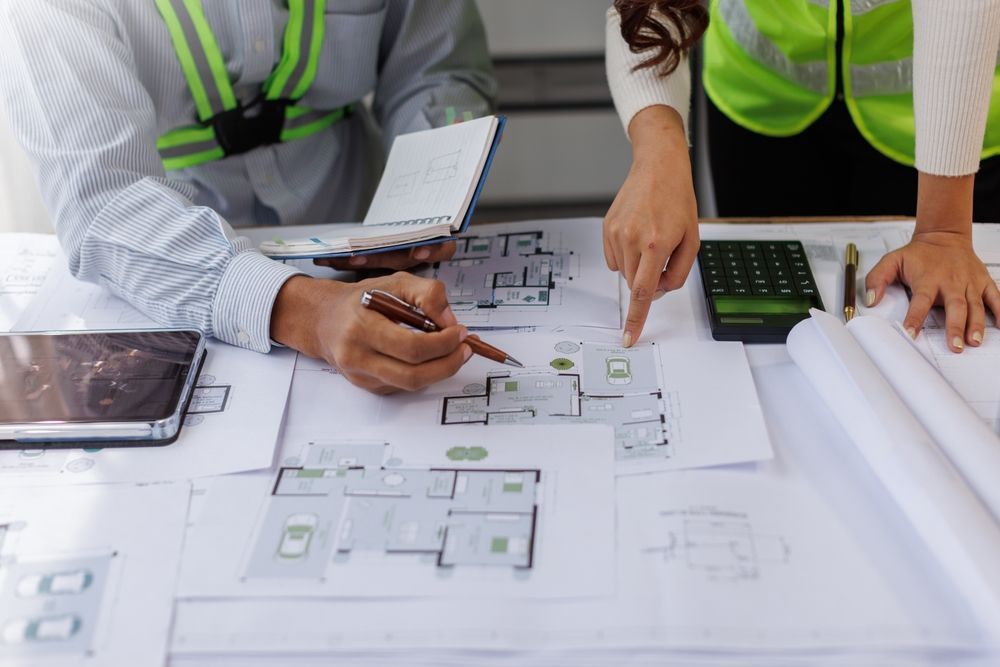 Team reviewing architectural floor plans on a desk with tablet and calculator