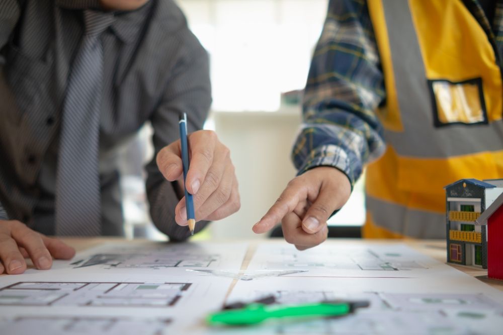 Two people drawing plans on a table with a pen and pencil, wearing business and safety vests.