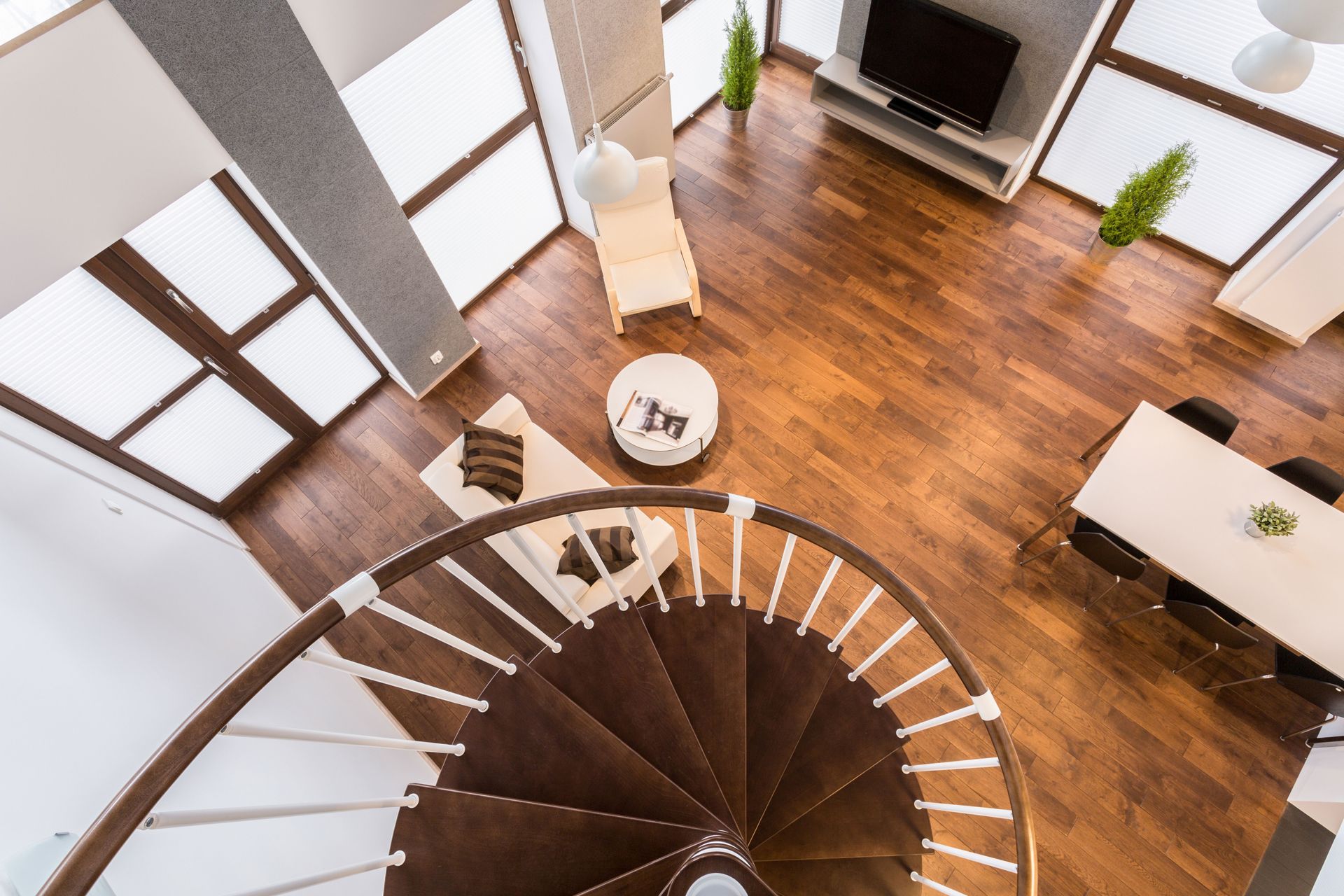 Modern living room with a spiral staircase, wood floors, white furniture, and large windows.