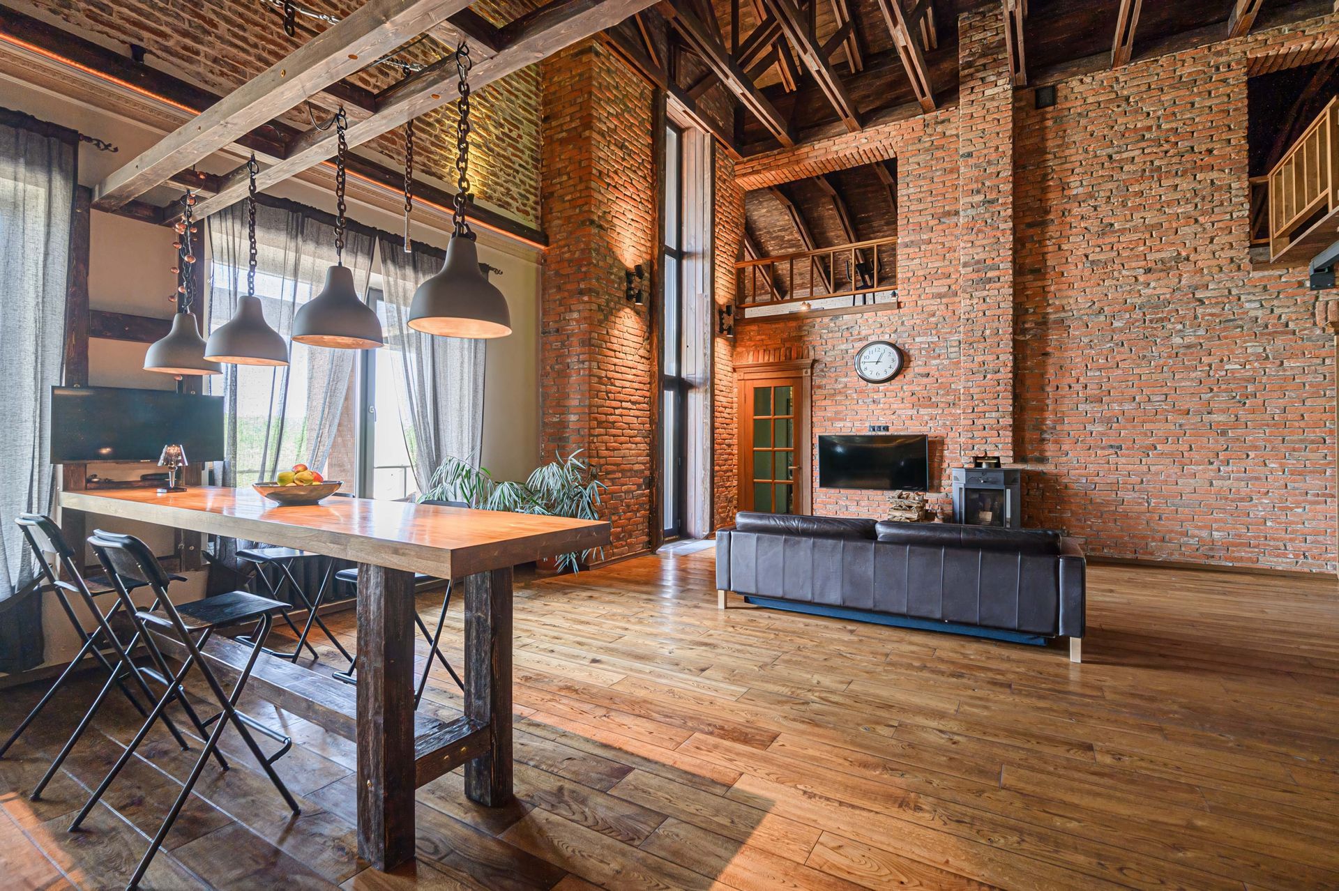 Loft-style dining room with exposed brick walls, wooden beams, and a long table under pendant lights.
