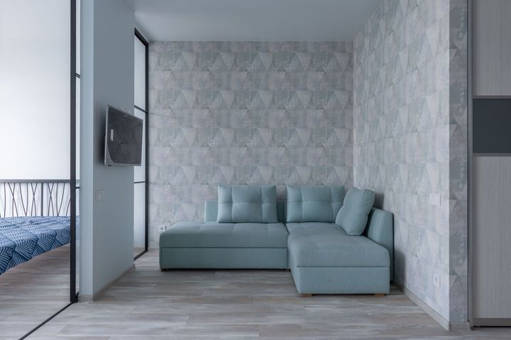 Modern living room with a light blue sectional sofa, geometric wallpaper, and wood flooring