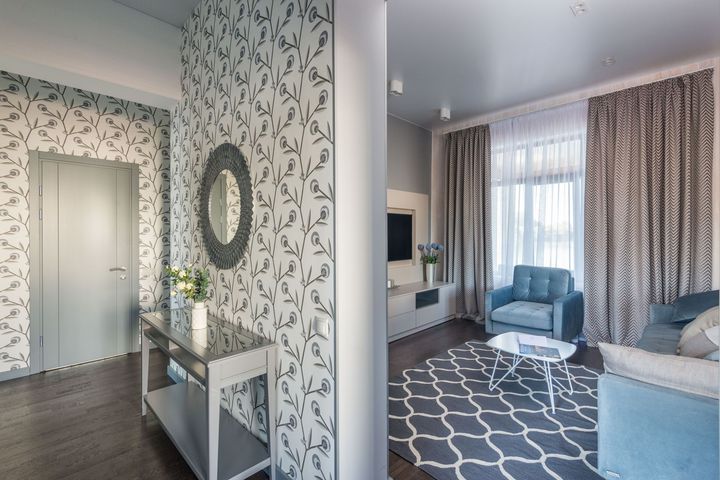 Hallway opening into a living room with blue chairs, patterned rug, and floral wallpaper