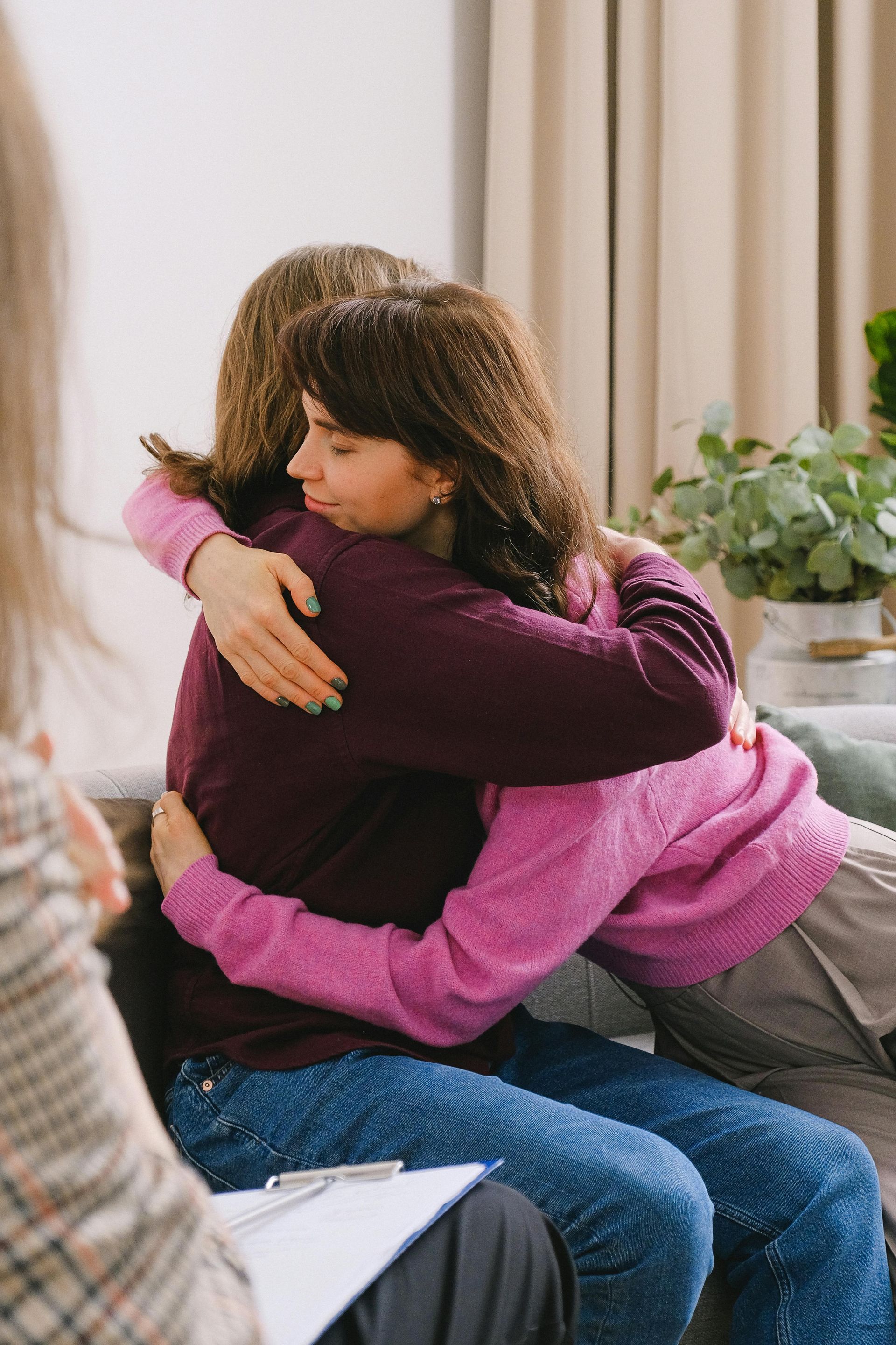 Two people hugging on a couch, one in a pink sweater and one in a maroon sweater.