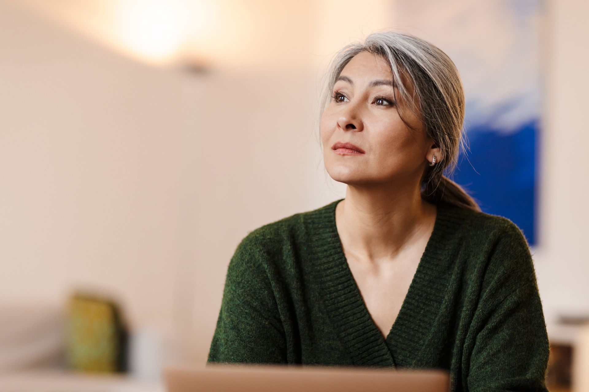 Woman with gray hair, wearing green sweater, looks upward, seated indoors.