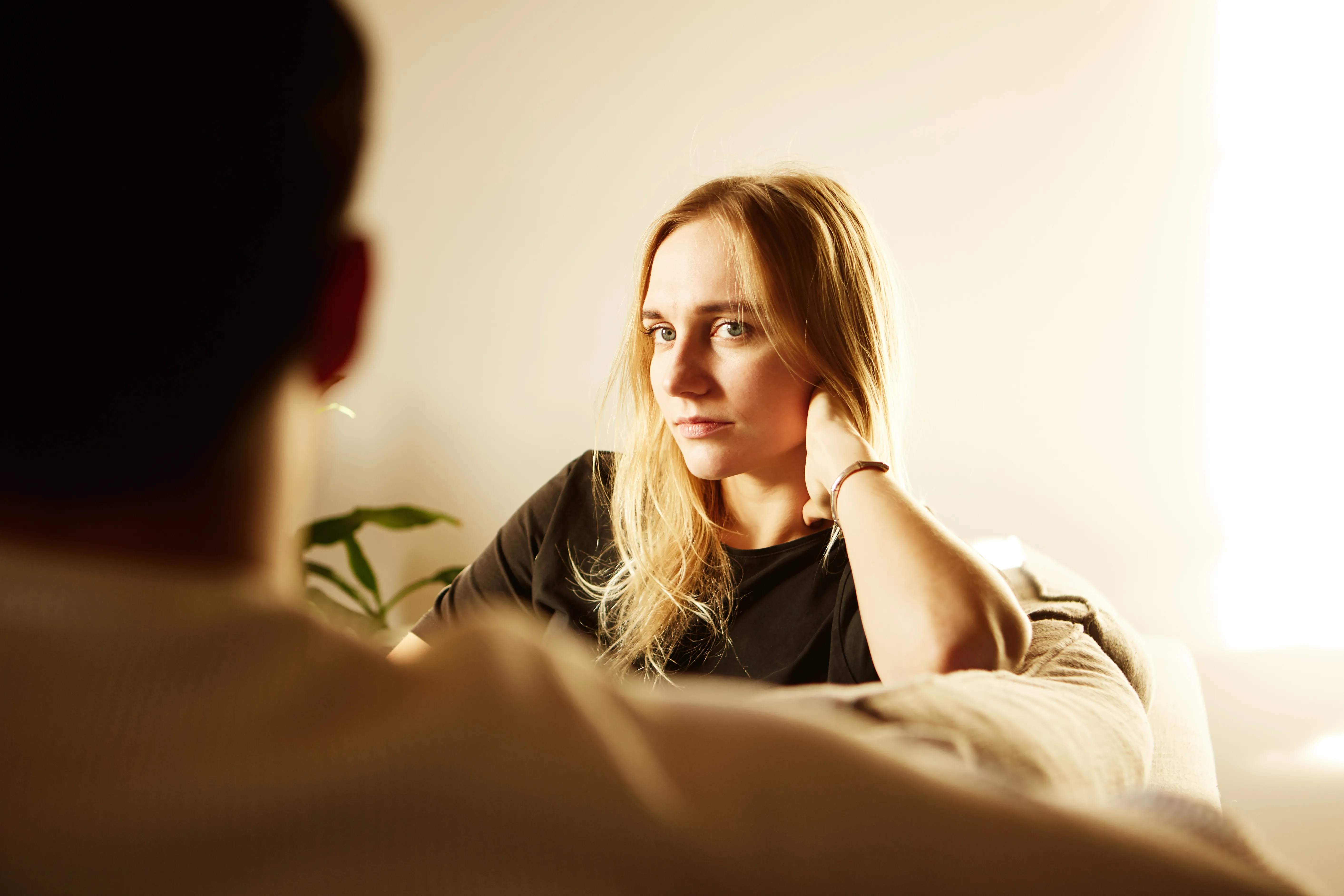 Woman with blonde hair looks at a man in a bright room. She rests hand on face.