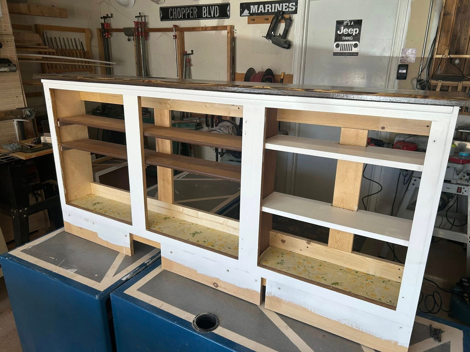 Wood cabinet with shelves, white frame, sitting on blue boxes, in a workshop.