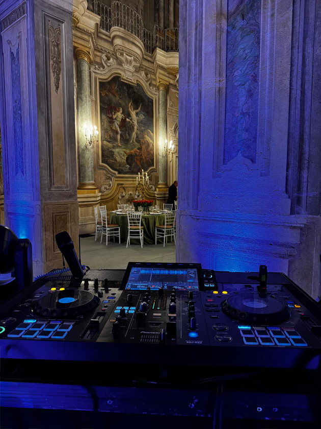 Il pubblico osserva un oratore su un palco illuminato di blu, con una console di missaggio audio in primo piano.