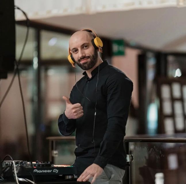 DJ in primo piano durante una serata/evento, con uno stile sportivo ma elegante