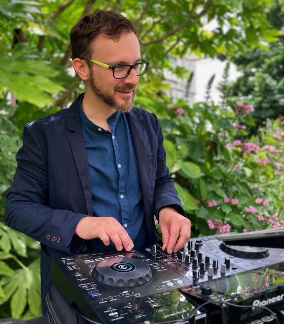 DJ in primo piano durante una serata/evento, con uno stile sportivo ma elegante