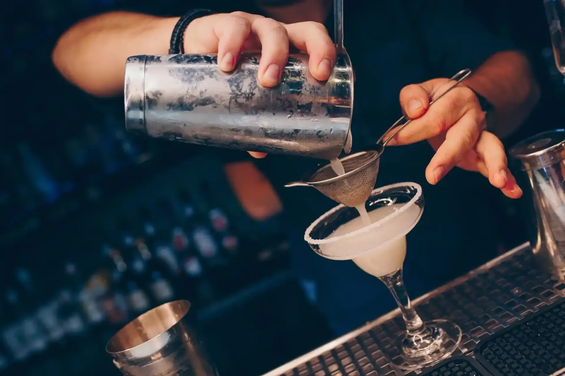 Un barista versa un cocktail attraverso un colino in una coppa in un bar