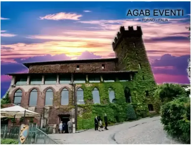 Castello in pietra con torre ricoperta d'edera al tramonto, cielo colorato sopra e persone che camminano su un sentiero.