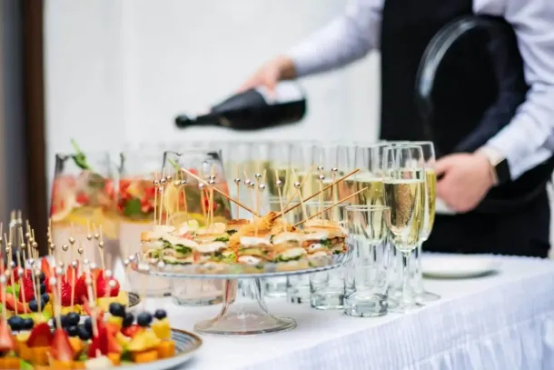 Il personale del catering versa spumante accanto agli antipasti e ai calici di champagne su un tavolo del buffet.