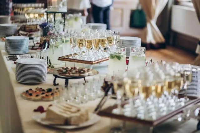 Tavolo a buffet con pasticcini, bevande e piatti impilati in occasione di un evento al chiuso con servizio di catering.