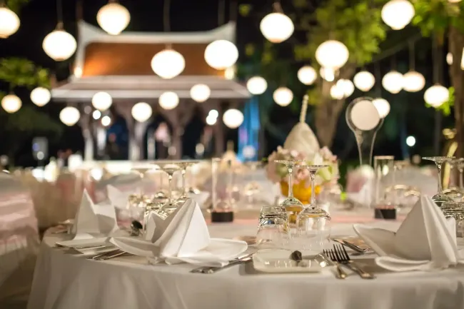 Elegante tavolo da pranzo all'aperto con tovaglioli bianchi, bicchieri e calde luci sospese di notte.