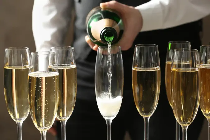 Una persona versa del vino spumante in un flûte tra diversi bicchieri da champagne già pieni.