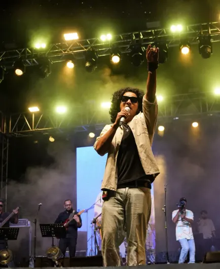 Cantante sul palco con microfono, braccio alzato sotto le luci intense del concerto e il fumo