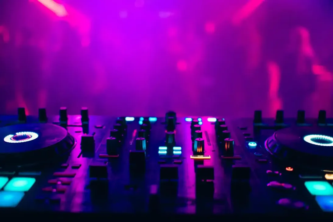 Mixer da DJ con luci blu e rosa scintillanti in un ambiente da discoteca.