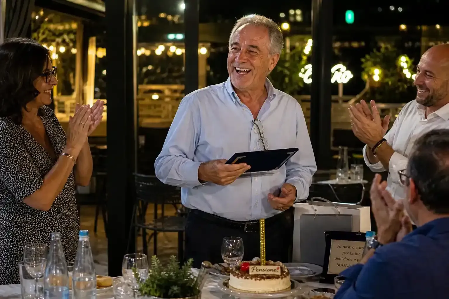 Durante una festa in un ristorante, le persone si sono riunite attorno a una torta mentre un oratore sorridente teneva in mano un tablet.