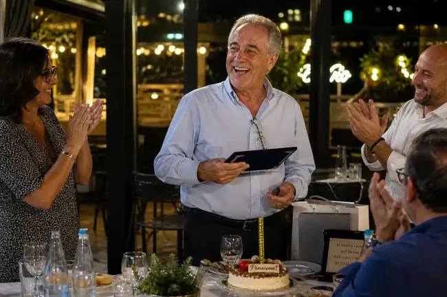 Un uomo fa un brindisi a un tavolo illuminato da candele mentre gli ospiti applaudono e sorridono.