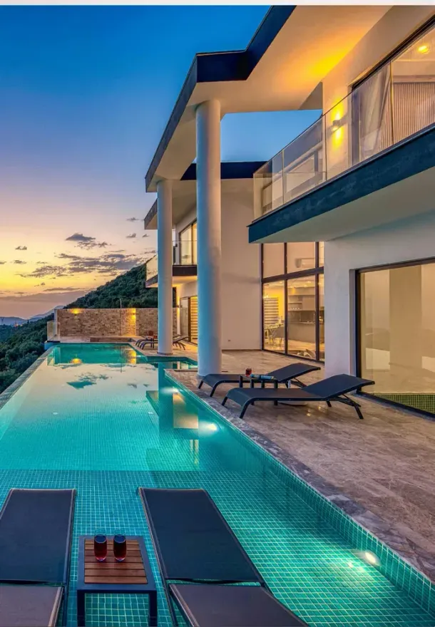 Villa di lusso con piscina a sfioro al tramonto, patio illuminato e vista sull'oceano.