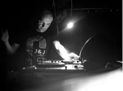 Un DJ si esibisce alla consolle in una scena scura, in bianco e nero e ad alto contrasto.