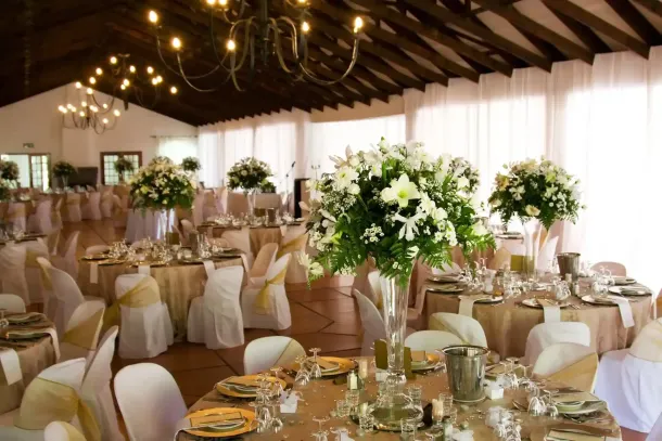 Elegante sala ricevimenti di nozze con tavoli rotondi, sedie bianche e grandi centrotavola floreali illuminati da luci calde.