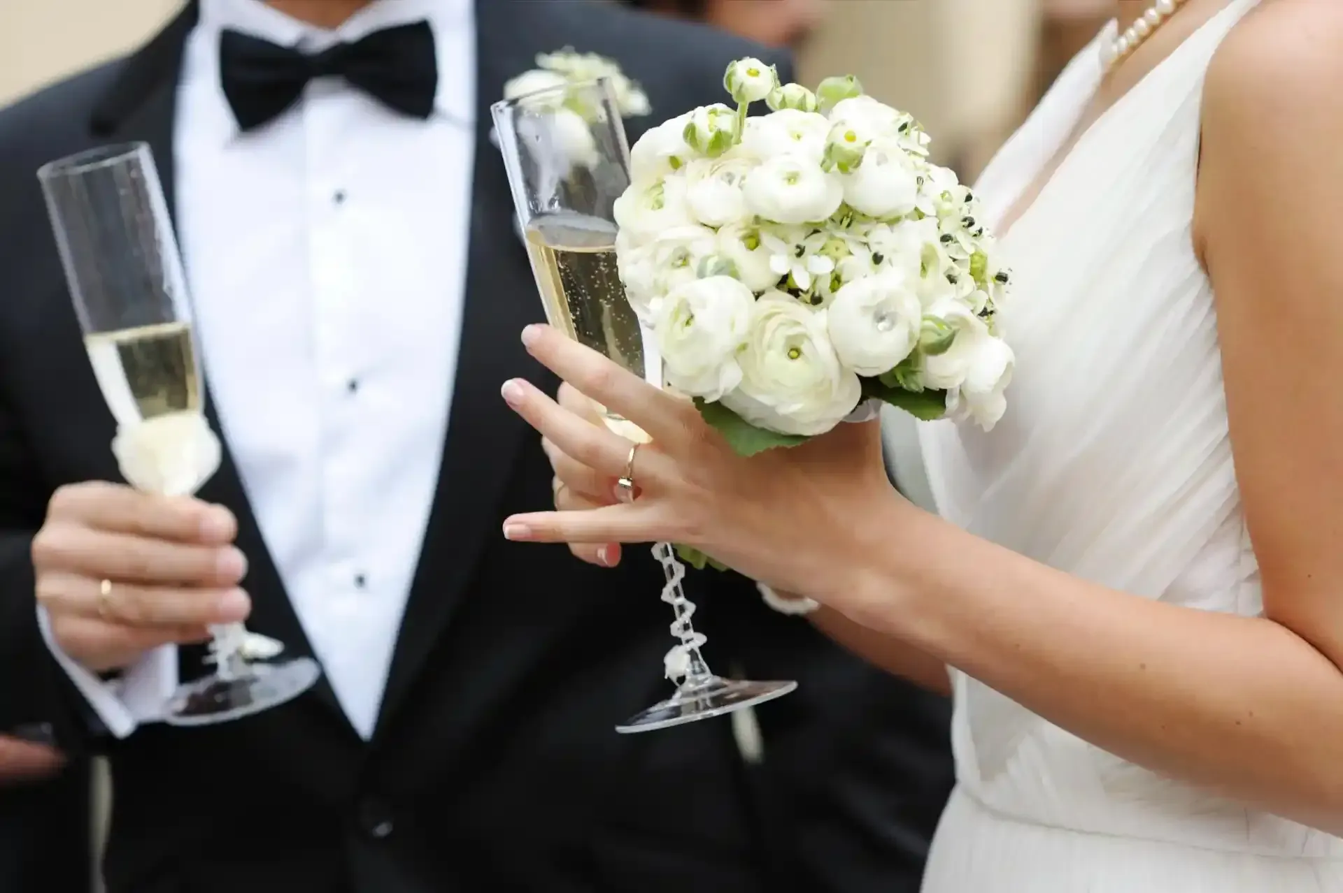 Gli sposi tengono in mano calici di champagne e un bouquet di rose bianche a un matrimonio.