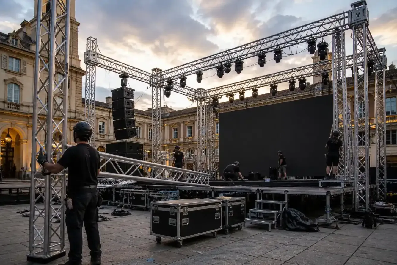 Palco per concerti all'aperto allestito in una piazza cittadina, con struttura per l'illuminazione, altoparlanti e un membro della troupe che regola l'attrezzatura.