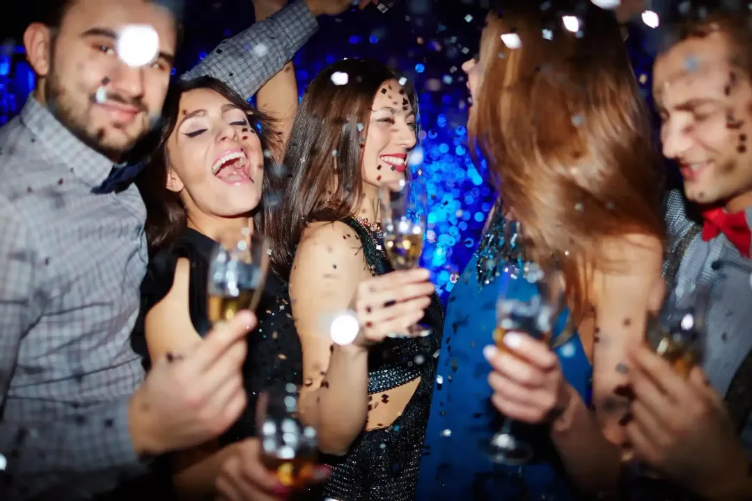 Amici a una festa vivace, sorridenti e con in mano drink tra luci blu e coriandoli.
