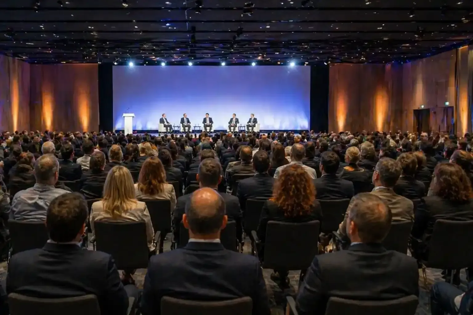 Pubblico seduto a una conferenza che ascolta un panel su un palco illuminato
