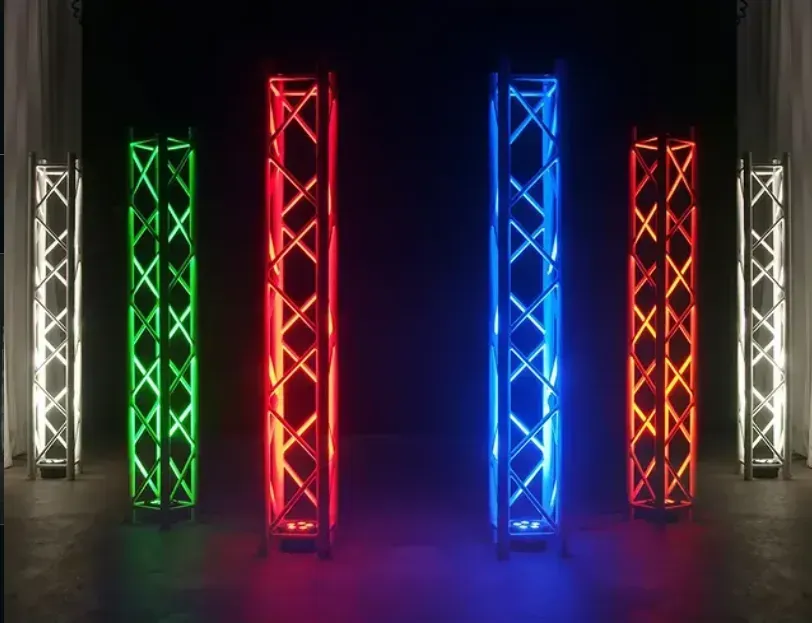 Cinque torri a traliccio illuminate di bianco, verde, rosso, blu e arancione su un palcoscenico buio