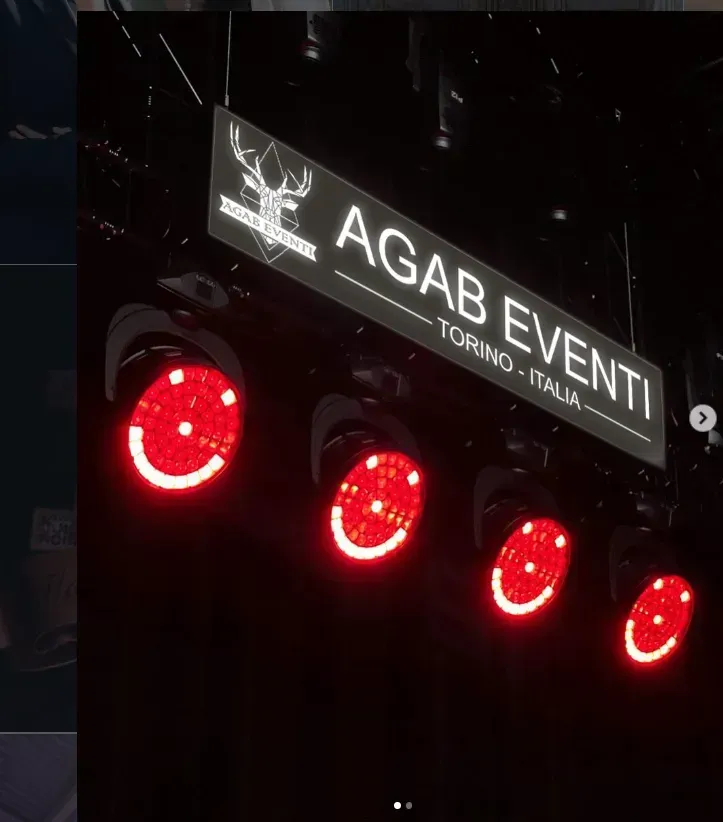 Insegna dell'evento AGAB sopra quattro luci rosse brillanti sul palco, in un locale buio.