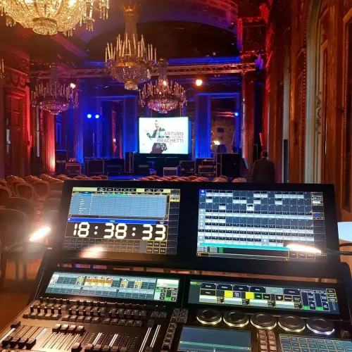 Vista dalla sala di controllo di una sontuosa sala da ballo con lampadari e uno schermo scenico illuminato di blu e rosso.