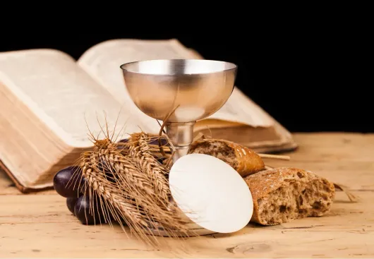 Pane della comunione, calice per il vino e Bibbia aperta su un tavolo di legno.