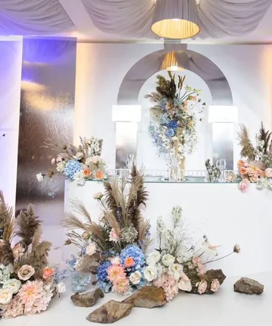 Elegante sfondo floreale per eventi con drappeggi bianchi, fiori dai colori pastello e uno specchio dorato al centro.