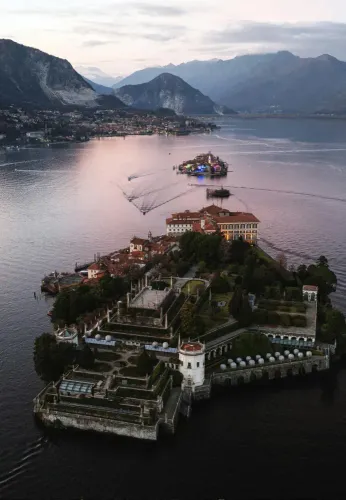 Tenuta su un'isola affacciata su un lago tranquillo al crepuscolo, con le montagne sullo sfondo e luci colorate sull'acqua.